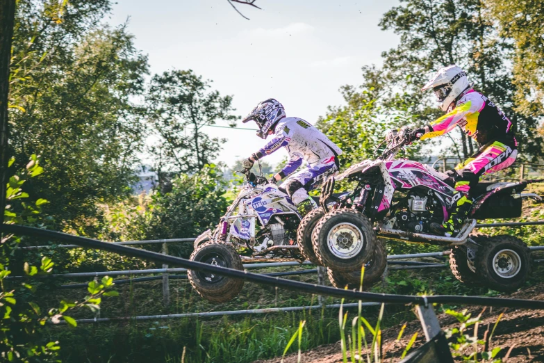 two people riding four wheelers through the woods