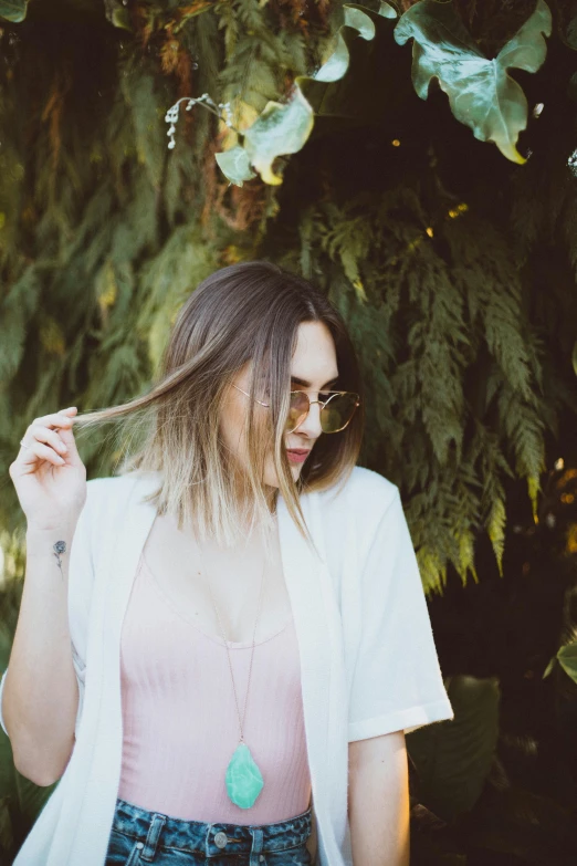 woman in the woods is wearing sunglasses and a white shirt