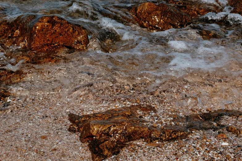 a sandy shore with rocks and water and pebbles