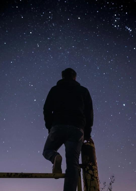 man standing on railing overlooking night sky with stars in sky