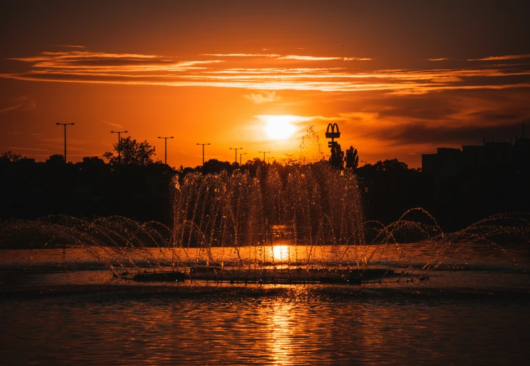 a spouting fountain is silhouetted against a colorful sunset