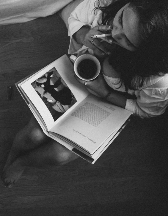 a woman holding an open book next to a coffee cup