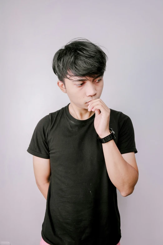 a boy in black t - shirt with finger near mouth and both other hand on mouth