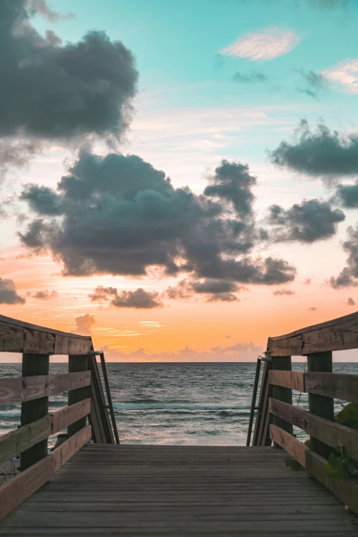 a boardwalk extending into the ocean with an orange and blue sunset in the distance