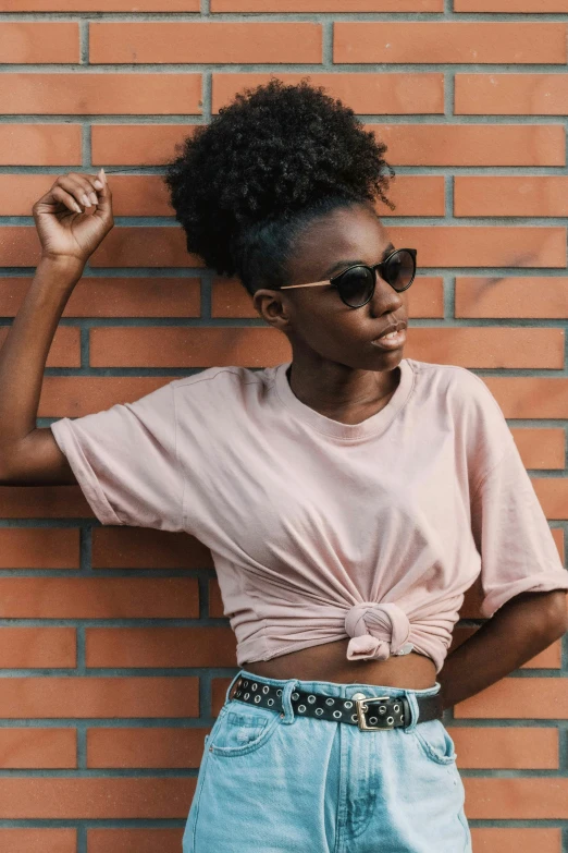 a woman in a pink shirt standing against a brick wall