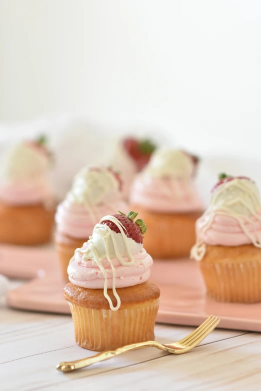 small cupcakes with vanilla frosting and a strawberry on top