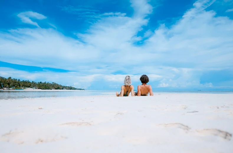 two people are sitting on the beach looking at the water