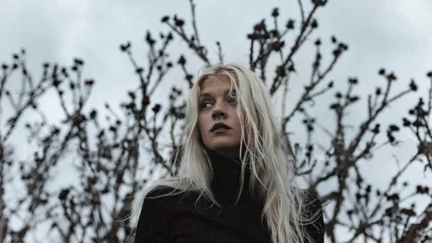 a woman with blonde hair standing next to a tree