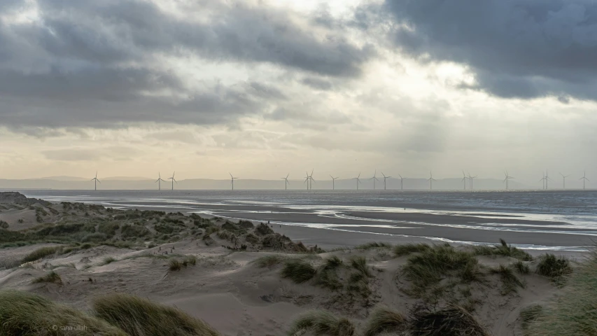 some wind mills and a long beach under a cloudy sky