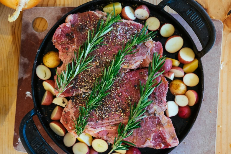 two pork chops in a pan with potatoes and other vegetables