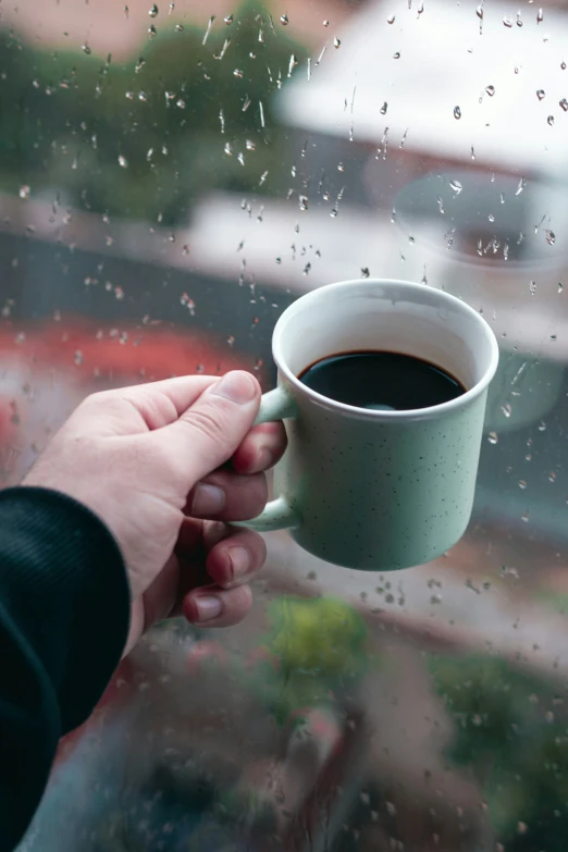 there is a person holding a coffee cup and a window with the rain coming in