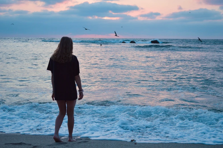 a woman standing on the beach looking at the ocean