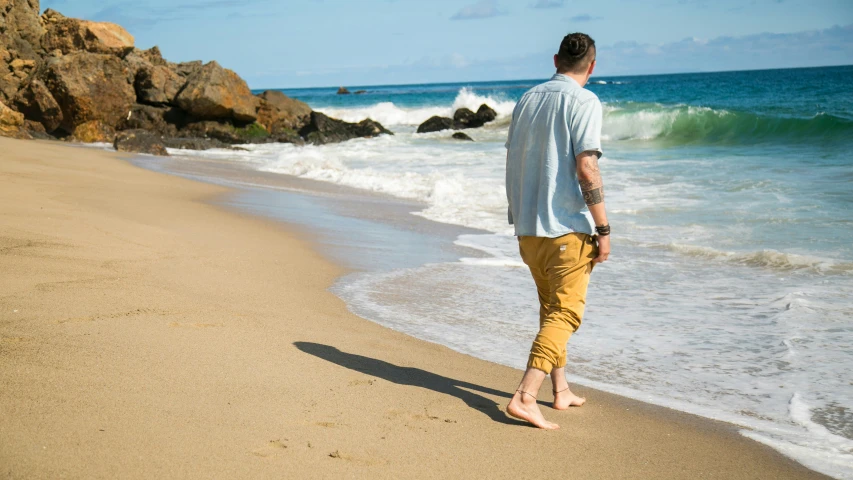 a man walking on a beach with his feet in the sand