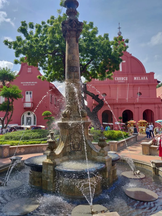 people walking around a small plaza with a water fountain in front of a large building