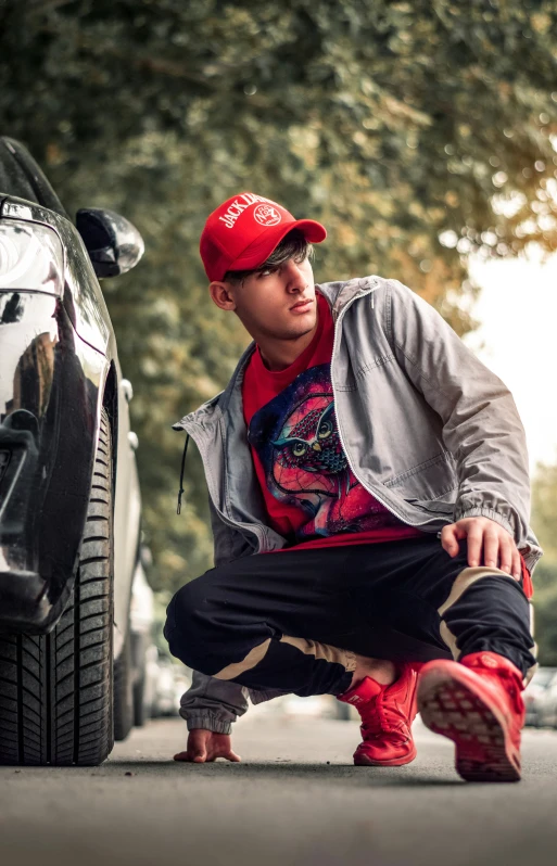the man is kneeling beside a car wearing a red hat