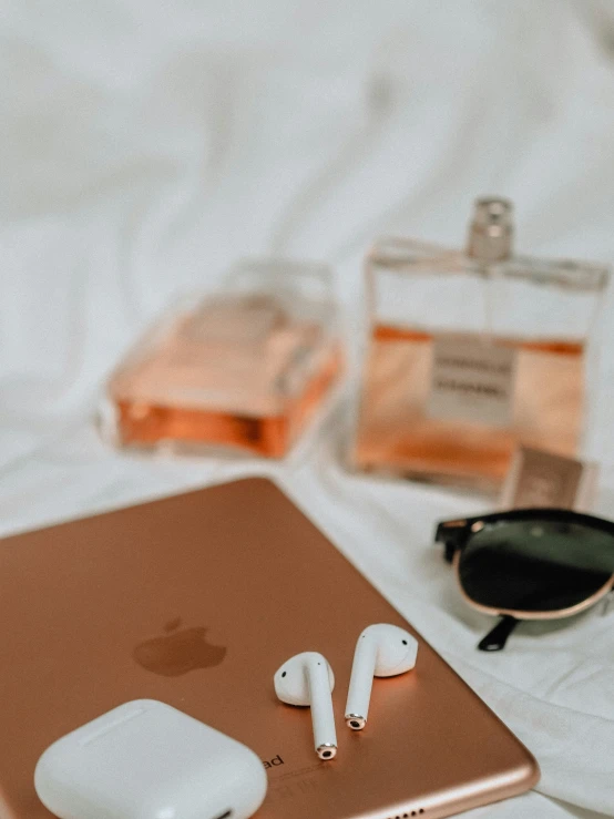 a pair of headphones, eyeglasses, and an apple ipad on a bed