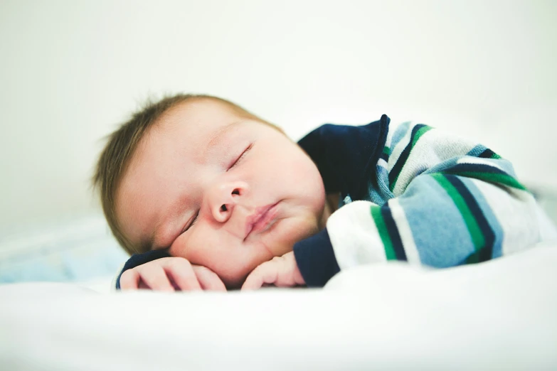 a baby sleeping in a blue and green blanket on top of a bed