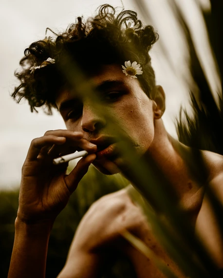 the young man with the flower in his hair smokes a cigarette