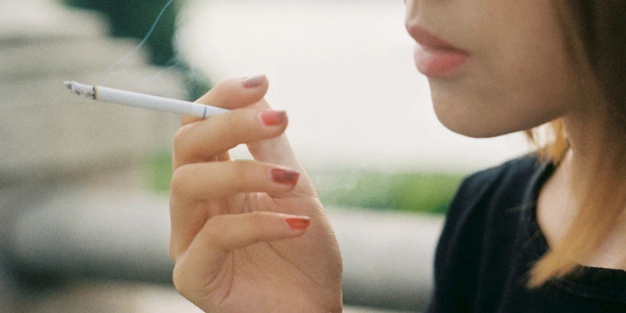 a young woman holding a cigarette and smoking an e - cig