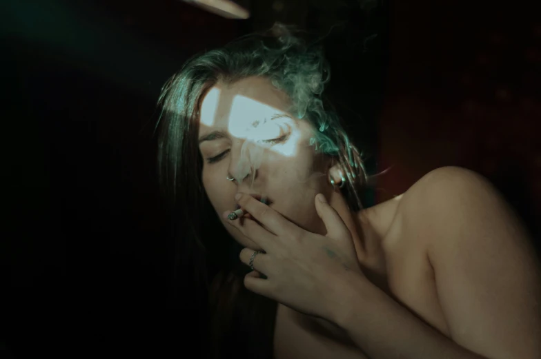 a woman is sitting in the dark smoking a cigarette