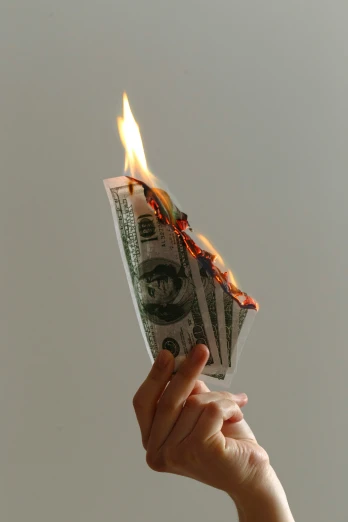 a man's hand holding up some money with fire coming from it