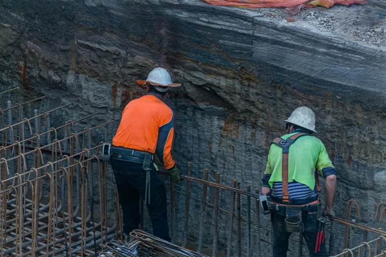 two construction workers wearing safety vests and hard hats near a large rock wall