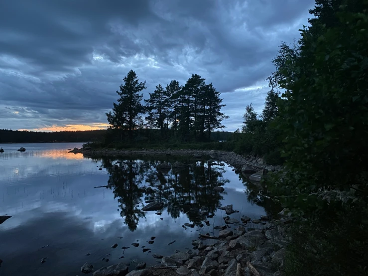 a small lake and trees at twilight with the sky in the background