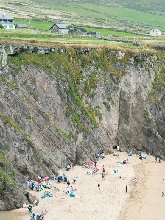 a group of people gathered together on the beach in front of a cliff