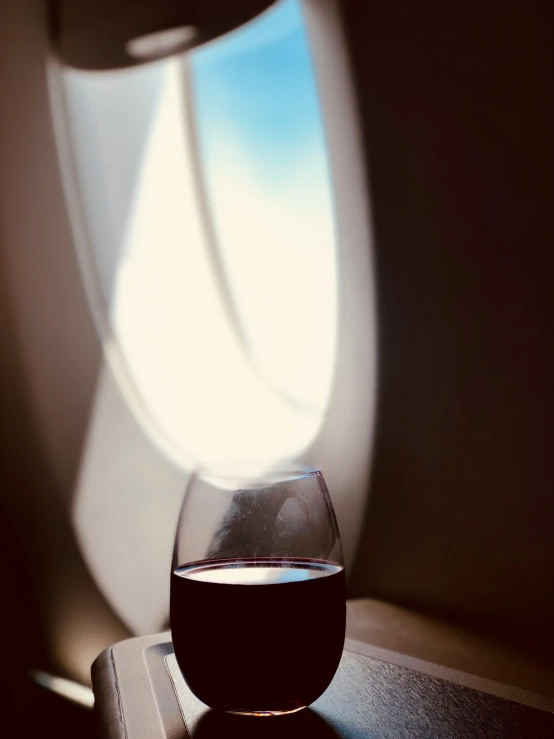 a glass sitting on top of a table next to an airplane window
