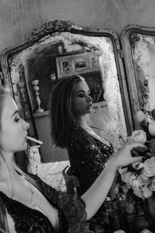 two women are drinking cigarettes near a mirror