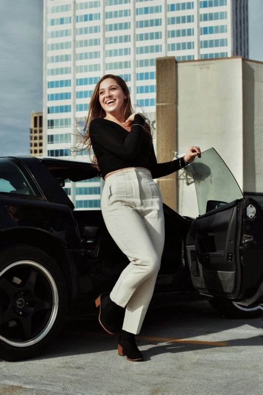 woman in white pants leaning into the side door of a black car