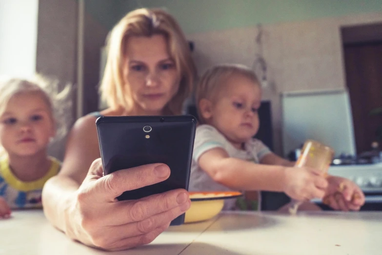 a woman is holding an iphone while two small children watch