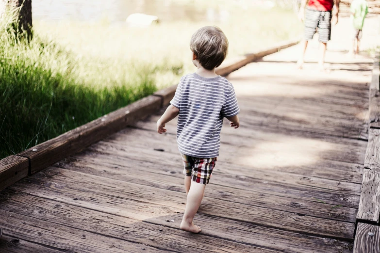 a small boy walking down a wooden boardwalk