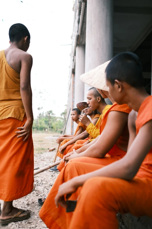 men sitting outside in orange robes with their hands in their pockets