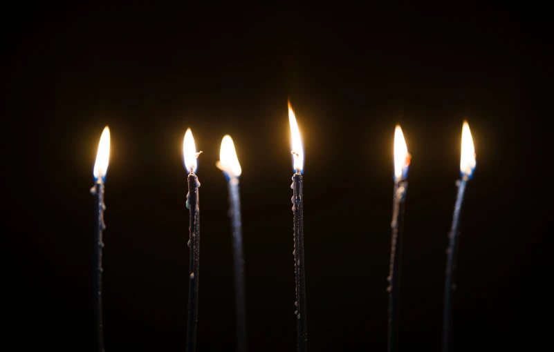 a number of candles with one lit on a stick