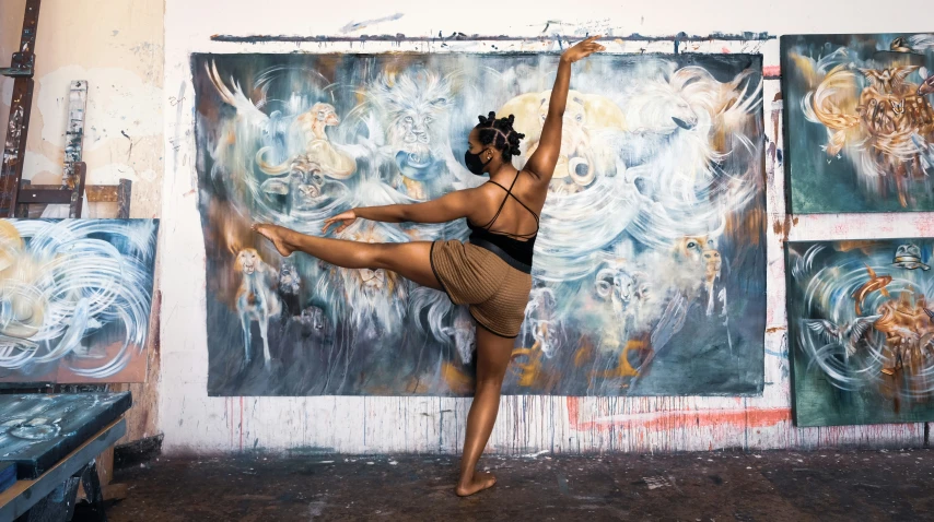 the dancer is doing an artistic pose in front of many paintings