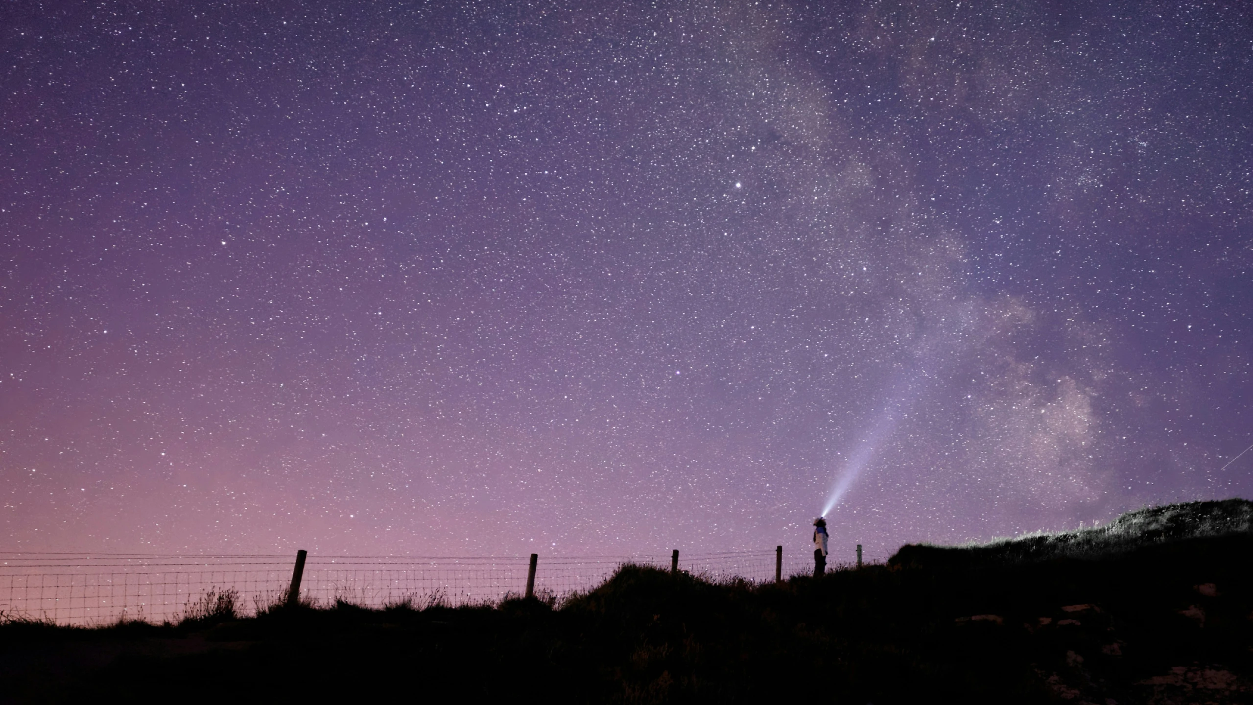 a fenced in field with stars and a night sky