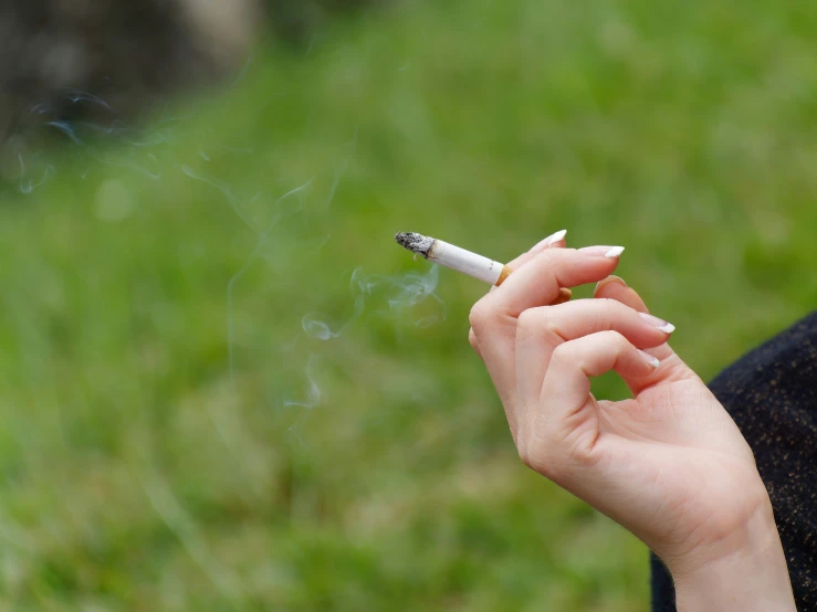 a woman is smoking a cigarette in the grass