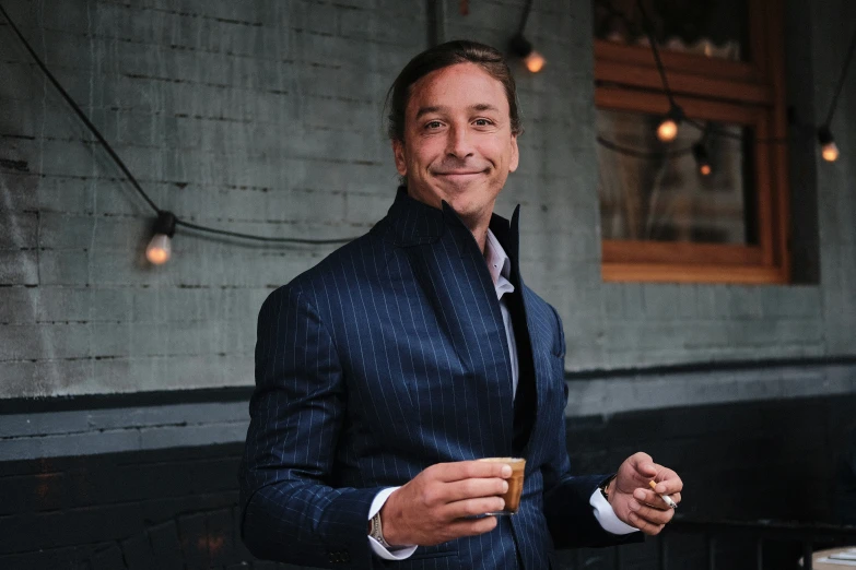 man in dark suit holding a drink and smiling