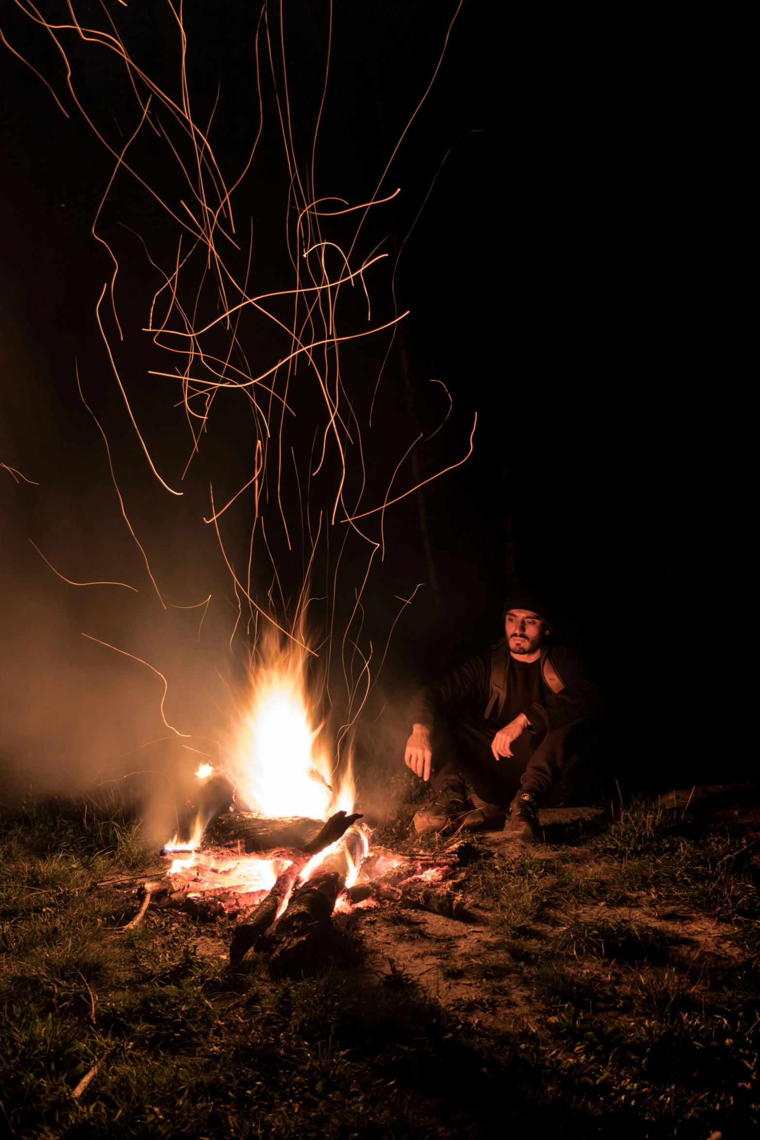 a man sitting next to a campfire at night