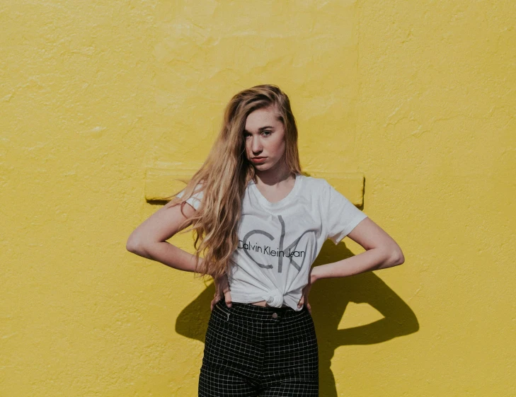 a woman standing against a yellow wall wearing black shorts