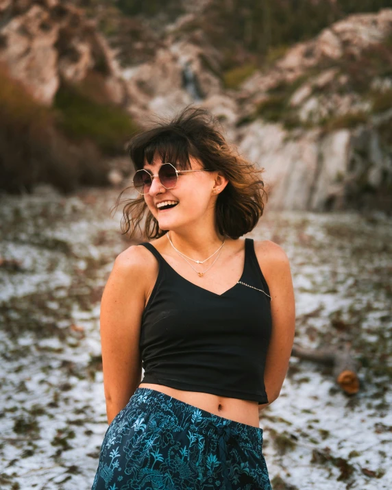 a woman in a black top with sunglasses standing in the mud