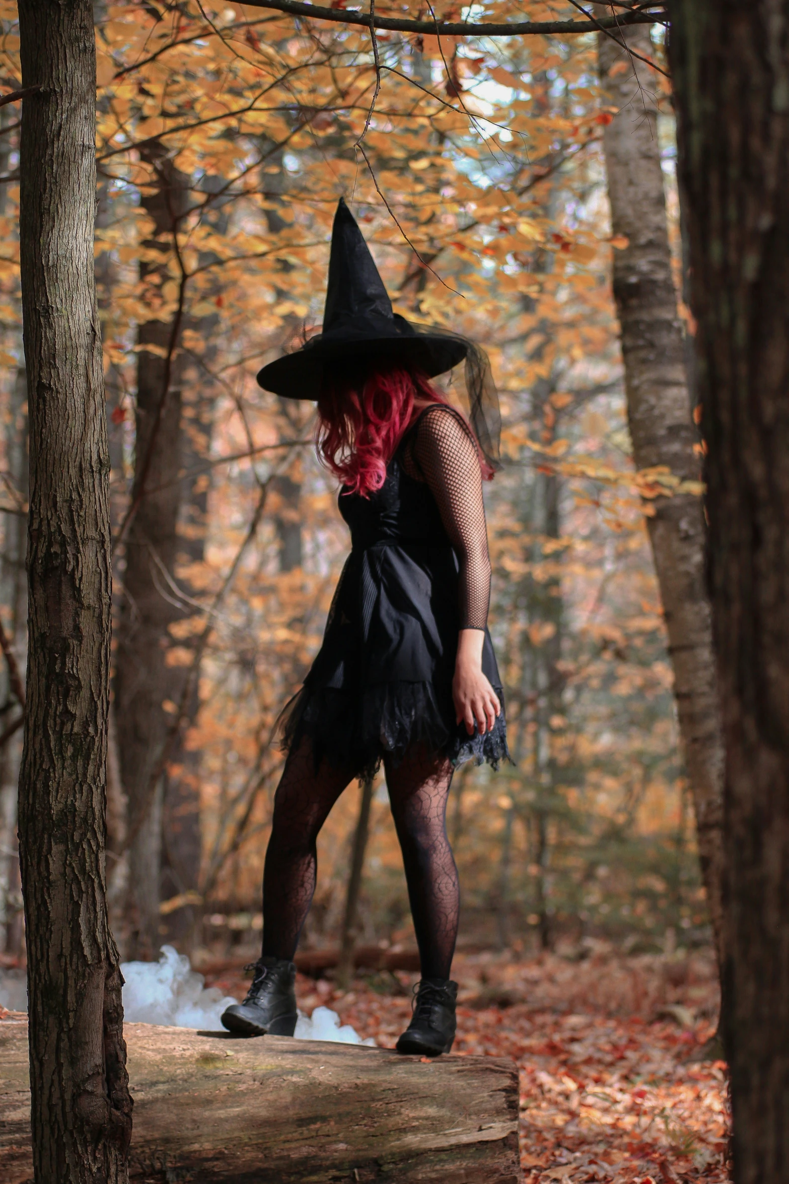 a woman in black clothes, hat and boots poses on log