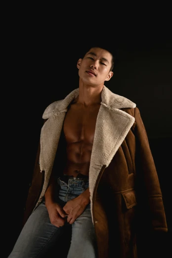 a shirtless man poses with his shirt down in a jacket