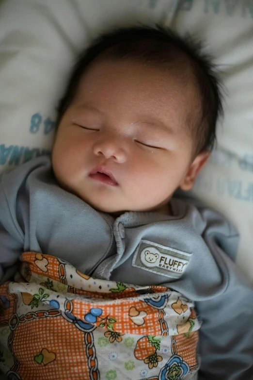 a baby is sleeping on the bed wearing a gray jacket