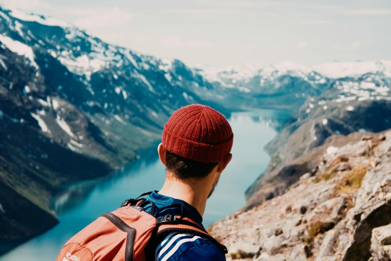 man in red hat and backpack looking over a valley