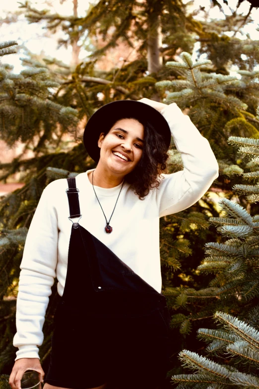 a woman wearing black suspenders standing in front of trees