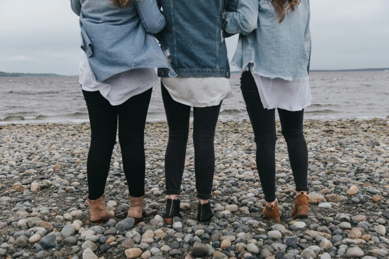 three women standing on top of a rocky beach near the ocean