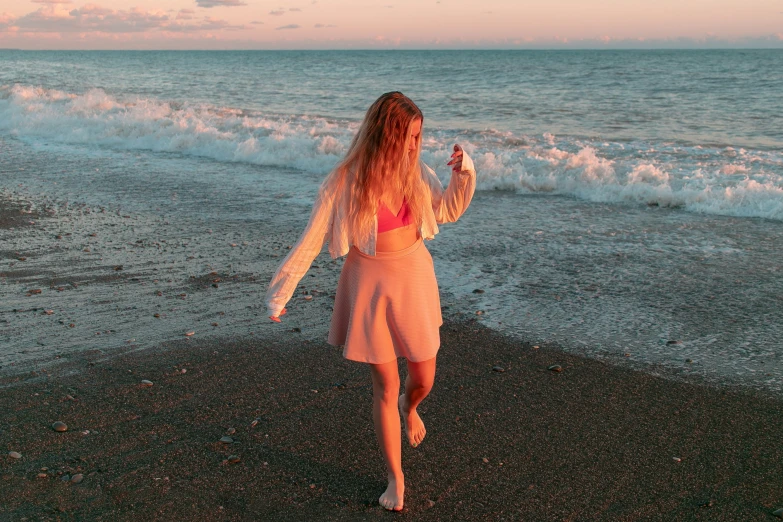 the girl in a pink dress runs along the shore as she holds her cellphone up to take pictures