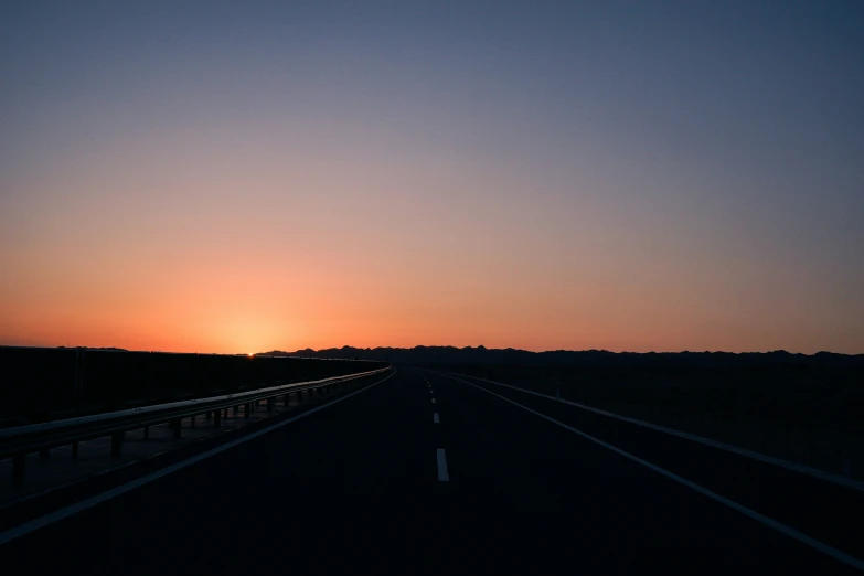 an empty highway at sunset with the sun setting in the background